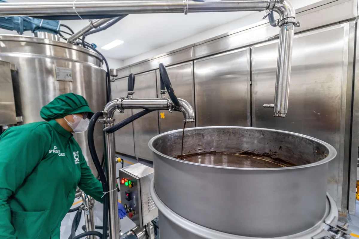 Liquid chocolate flowing into a stainless steel tank as a CAU production team member checks the controls